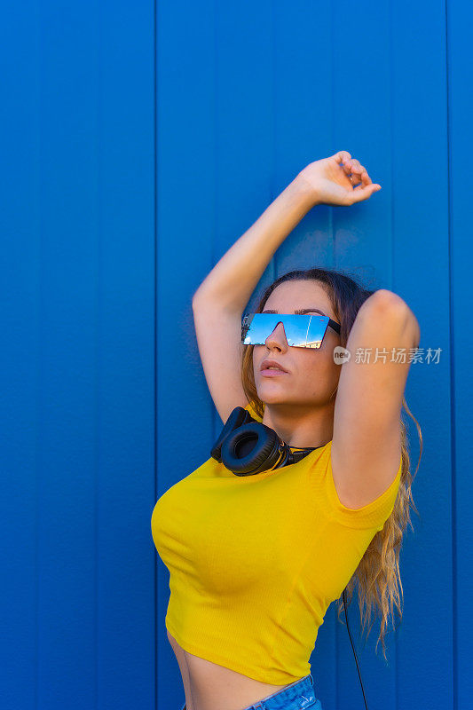 生活方式，金发白种人女孩黄色t恤蓝色背景。戴着耳机的Dj女孩为techno、house party或session海报做宣传